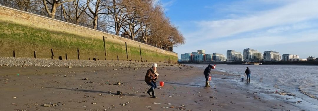 volunteers on the shore of the River Thames with blocks of flat in the distance
