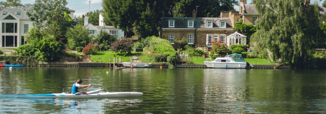 Landscape image of a rower, boats and a house by the water