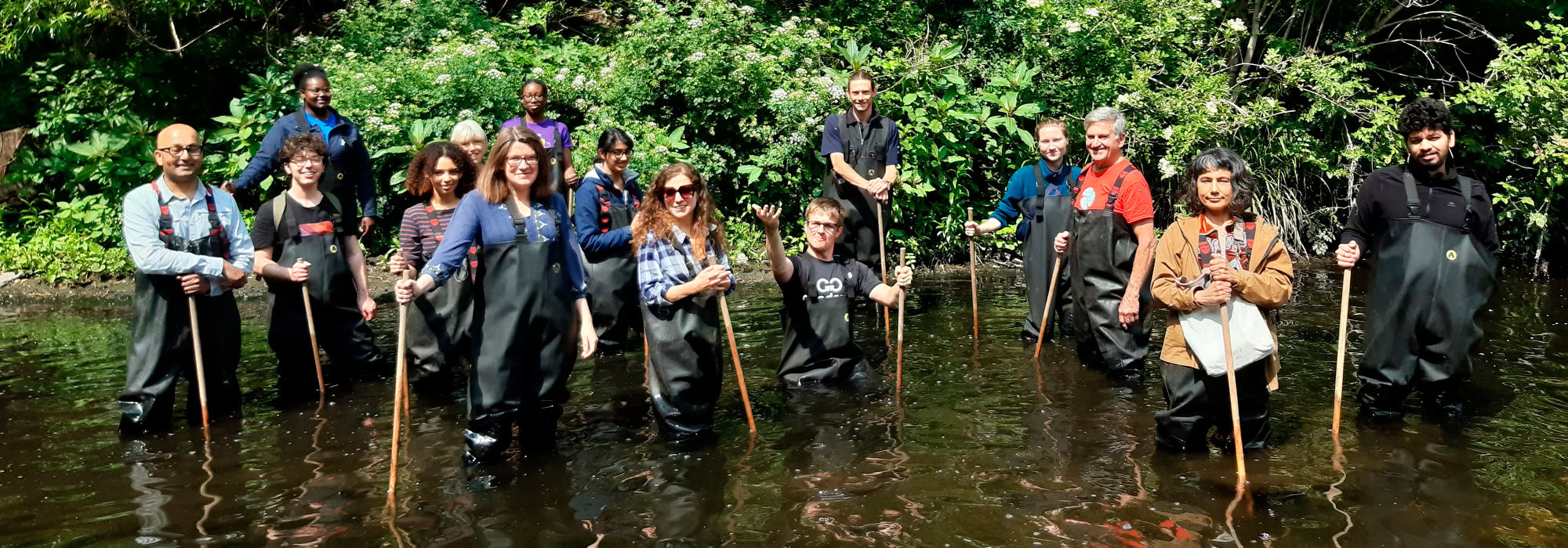 15 volunteers in waders standing knee deep in a river facing the camera and smiling